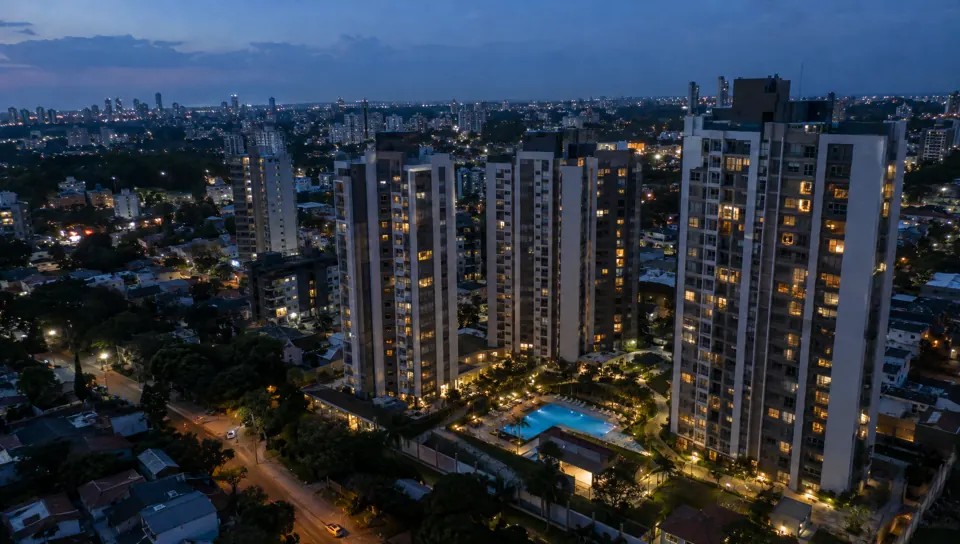 Render 3D ilustrativo aéreo de empreendimento residencial na hora azul, com janelas e piscina iluminadas